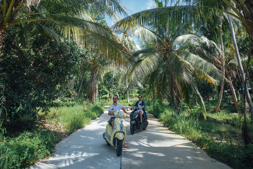 两个男人在热带岛屿的棕榈树上骑着摩托车棕榈树林路上骑图片