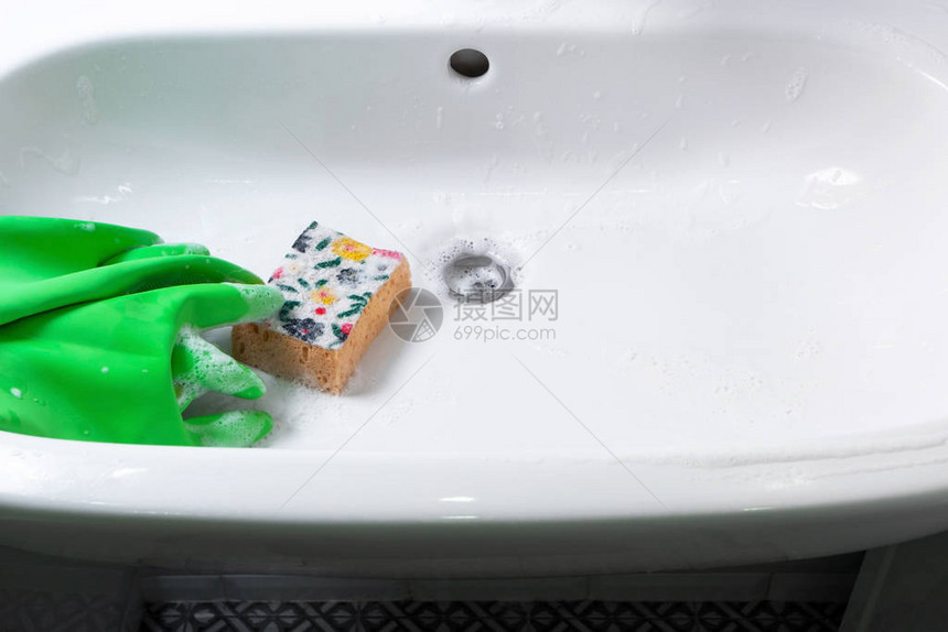 绿色橡胶手套和黄色海绵躺在陶瓷洗浴盆上图片
