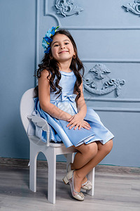 一个穿蓝色裙子的小孩穿着蜜蜂高跟鞋坐在白椅子图片