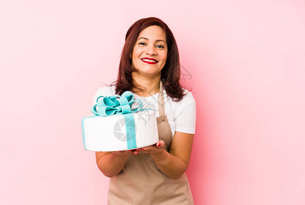 中年的拉丁女人拿着蛋糕在粉红背景上独处图片