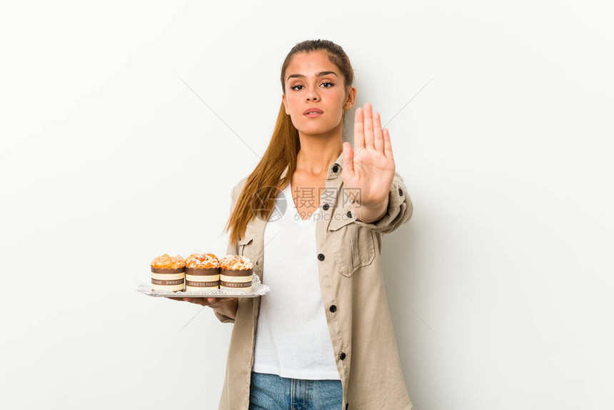 年轻caucasian女人拿着甜蛋糕站着伸展的手显示停图片