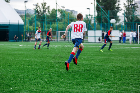 穿着白色和蓝色运动服的男孩在球场上踢足球图片