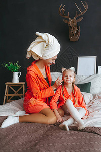头戴毛巾的微笑妈在床上在家笑着的女儿脸上涂白霜家庭护理图片