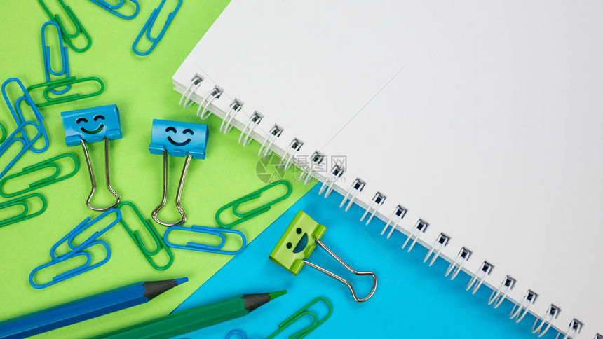 记事本上的绿色和蓝色办公回形针微笑活页夹和铅笔绿色和蓝色背景上的办公用品打开桌上的螺旋笔记本知识或教图片