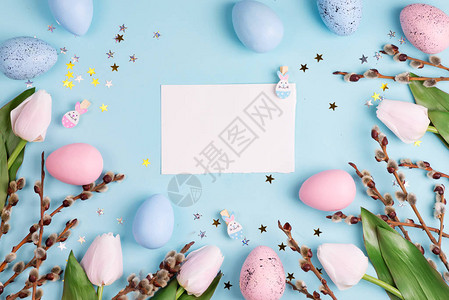 复活节柳花环白色郁金香和蓝色背景上的蓝色粉红色复活节彩蛋与纸顶视图片