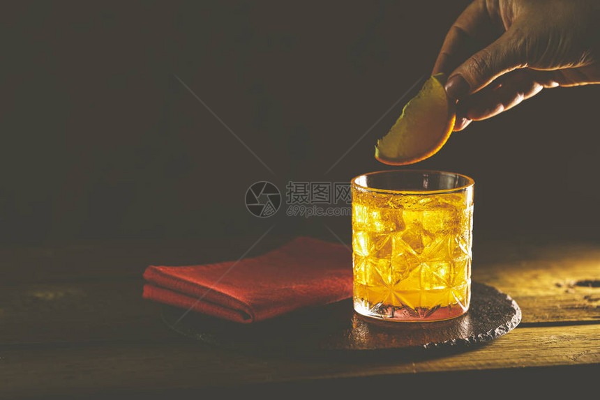 女人手装饰玻璃的橙片酒精鸡尾酒negroni与杜松子酒金巴利马提尼罗索和橙子一起饮用图片
