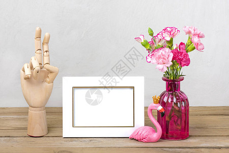 花瓶中的小彩色粉红康乃馨白相框火烈鸟图木桌上的木手和灰墙图片