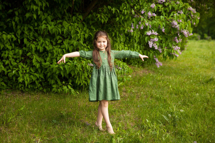 穿着绿色亚麻连衣裙的可爱女孩在公园里开着盛开的丁香花图片