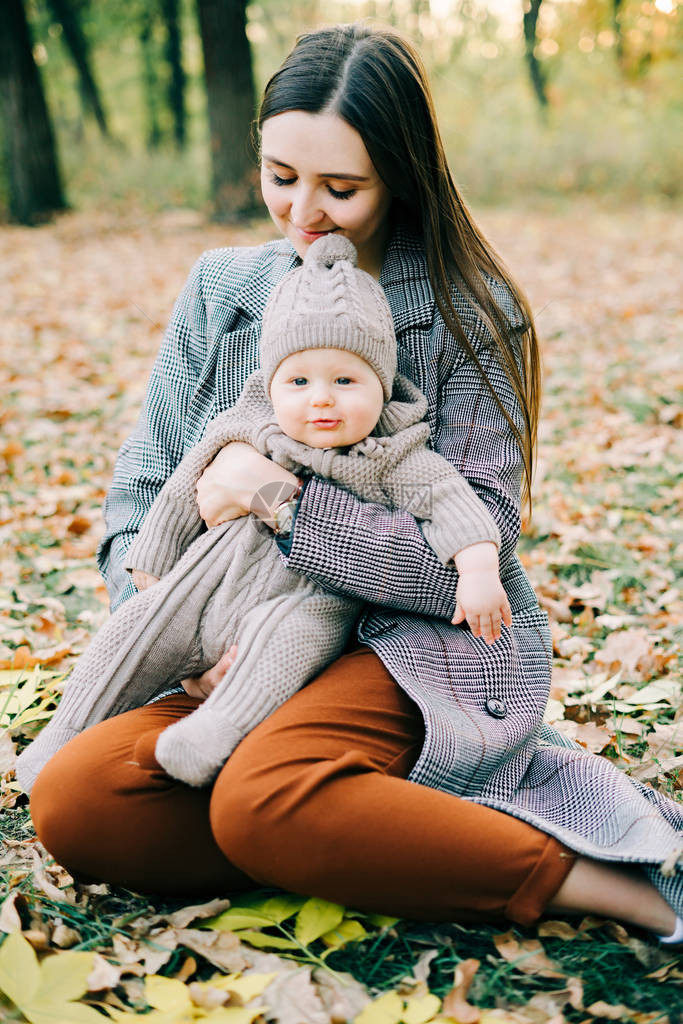 一位母亲在公园里抱着一个穿着温暖连身衣的可爱小男孩图片