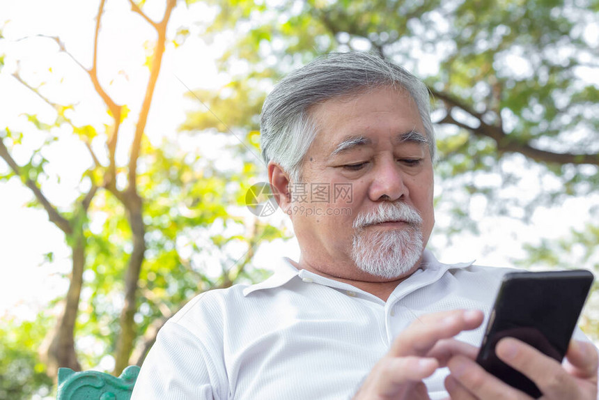 高级亚洲男子在公园使用智能手机和互联网在线阅读新闻或查看网站信息英俊的亚洲老人留着漂亮的胡须和小胡子老家伙看起来很严图片
