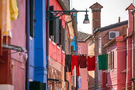 在意大利威尼斯著名的布拉诺岛有窗户和百叶窗的多彩房屋之间擦干衣服图片