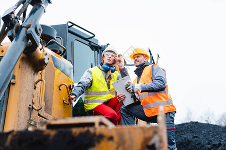 采石场的女和男工人在挖掘机上寻找一个超越地平图片