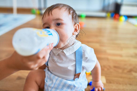 在幼儿园用喂养瓶子坐在地板上喝牛奶的适熟婴图片