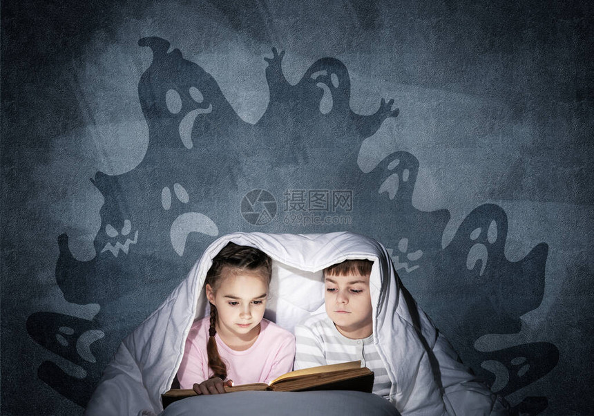全神贯注的小孩在床上看书兄弟姐妹一起躲在毯子下穿着睡衣的可怕孩子和灰色墙壁背景上的虚构怪物图片