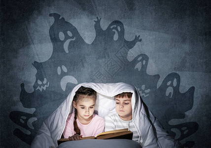 全神贯注的小孩在床上看书兄弟姐妹一起躲在毯子下穿着睡衣的可怕孩子和灰色墙壁背景上的虚构怪物背景图片