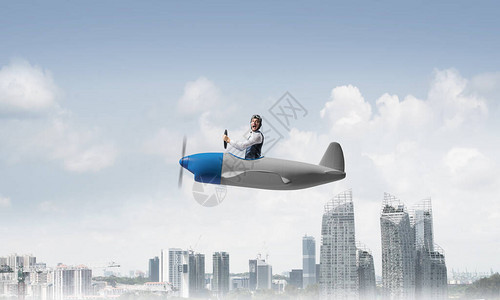 汽车帽和护目镜的商人驾驶螺旋桨飞机在市中心上空图片