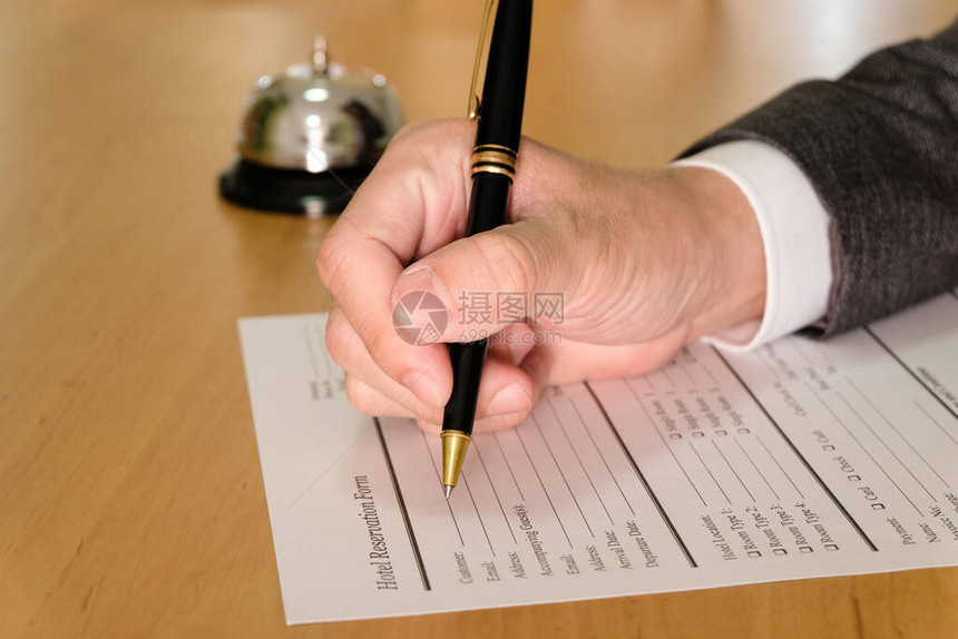 男士商务人士使用笔在接待处的酒店预订表上书写图片