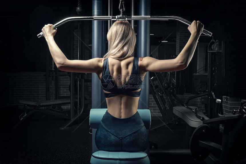 迷人的金发女郎在健身房锻炼背部颈部拉动头部健美健身的概念后视图片
