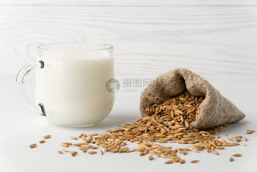 不含乳糖的乳制品在一个杯子里的燕麦牛奶和在白色背景上的一个小袋子里的谷物带有复图片