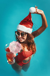 年轻漂亮的女人在游泳池里戴着圣诞老人的帽子图片