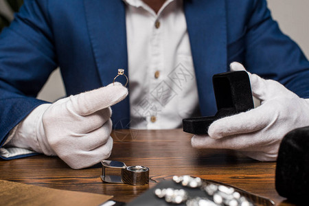 珠宝估价员拿着宝石戒指和灰色底面桌子上的盒子的珠宝鉴定背景图片