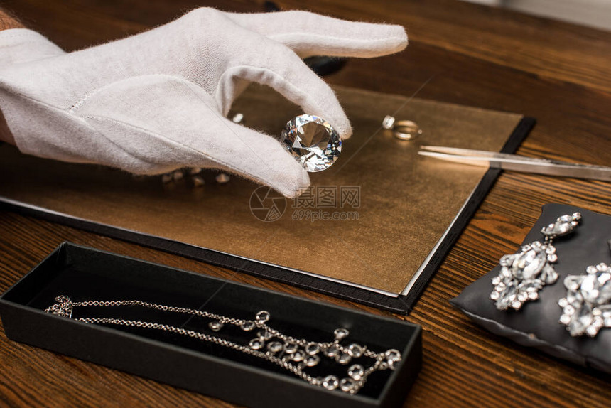 珠宝估价师在灰色桌子上的珠宝附近拿图片