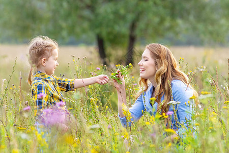 年幼母亲身着户外散装衣在夏日草原上取乐和摘花的美丽无助的女婴图片