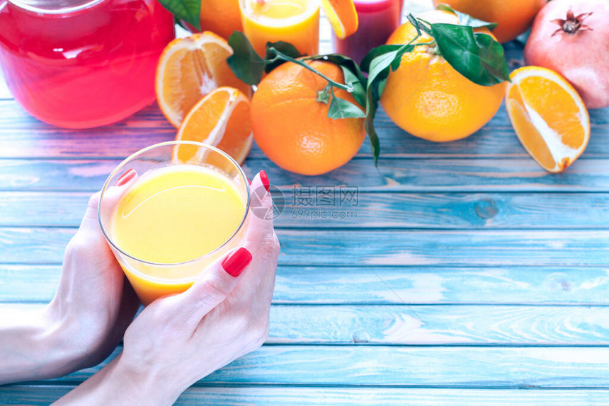 鲜榨橙汁在女手中蓝色木质背景上有图片