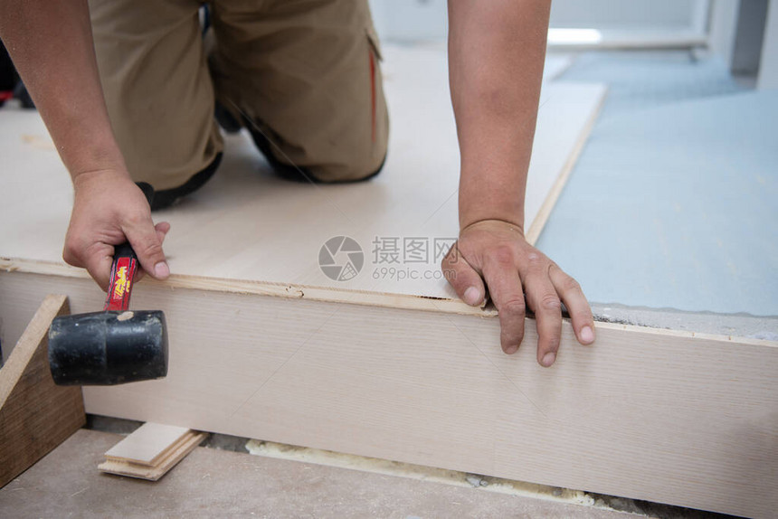 专业木匠在未完工公寓安装新的层状木制地板时使用橡胶锤图片