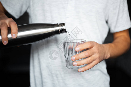 男手将水从钢制热生态瓶中倒入玻璃杯中图片