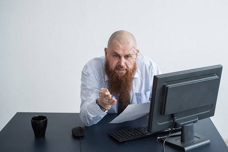 坐在桌子上看着报告和咒骂的秃头男子的肖像不高兴的酋图片