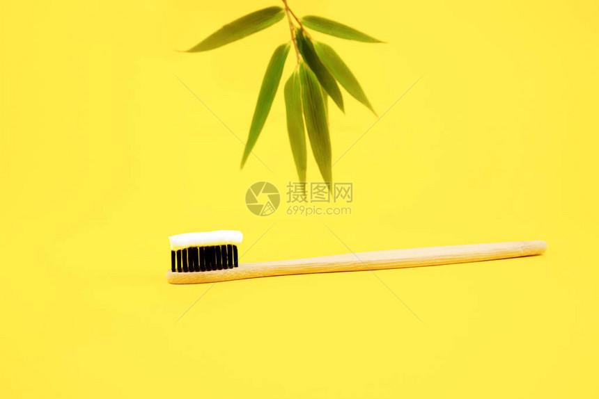 黄色背景上和背景竹叶中带有天然环保刷毛和白色牙膏的竹制天然刷回收产品口腔护图片