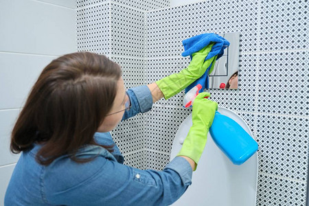 戴手套和抹布在卫生间打扫清洁和拉亮铬厕所的挂砖图片
