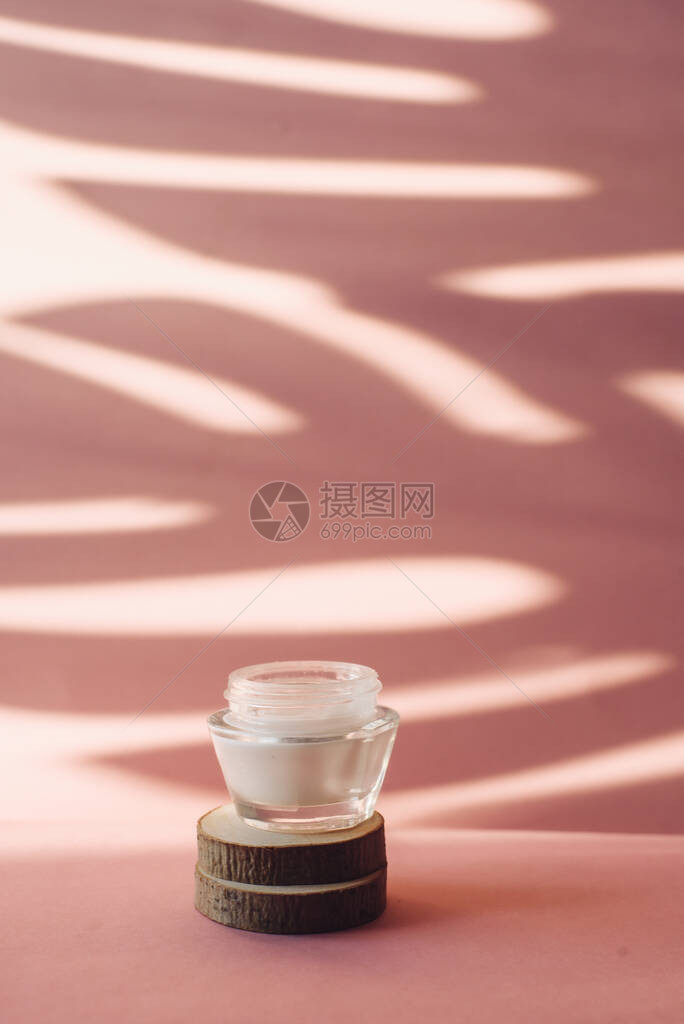 玻璃罐与白色保湿霜在木锯切在粉红色的背景棕榈叶热带阴影背景上的乳液图片