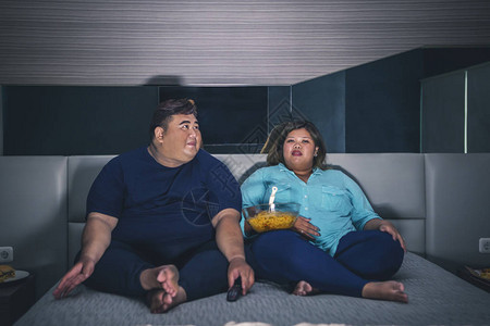 坐在床上的亚裔胖情侣在卧室里吃即图片