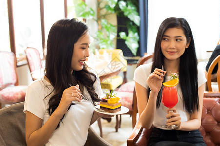 两位亚洲姐妹拍照并品尝美味的甜蛋糕和果汁图片