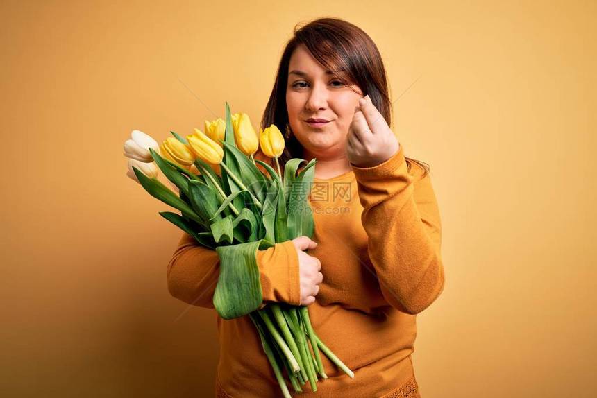 漂亮的大号女人在黄色背景上拿着浪漫的天然郁金香花束用手和指自信地表图片