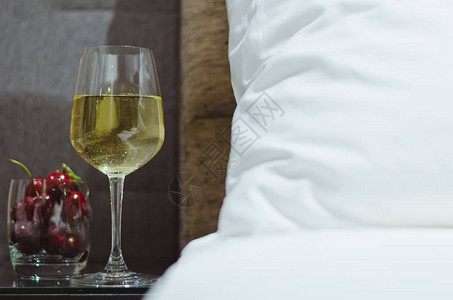 丽晶酒店一杯白葡萄酒和樱桃水果放在桌子上除了床背景