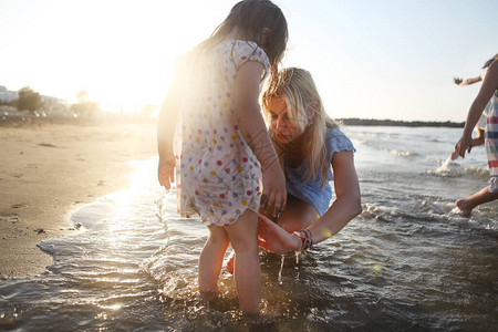 金发的年轻母亲在阳光明媚的夏日穿着鲜艳的波尔卡圆点洋装站在海上图片