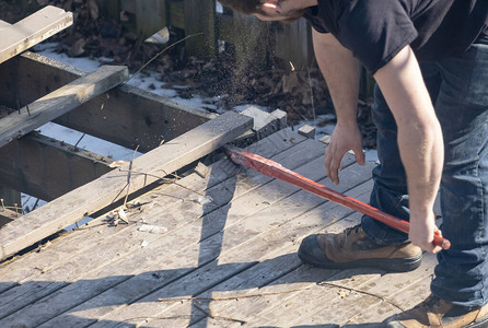 男子在后院用红撬棍拆除旧木甲板图片