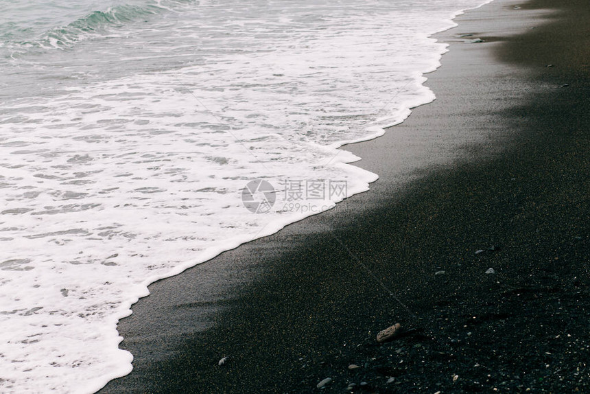 海浪随着黑火山沙落到岸边图片