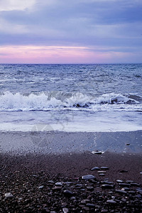 日落时的冷海卵石滩岸边的海浪与波浪的粉红色日落图片