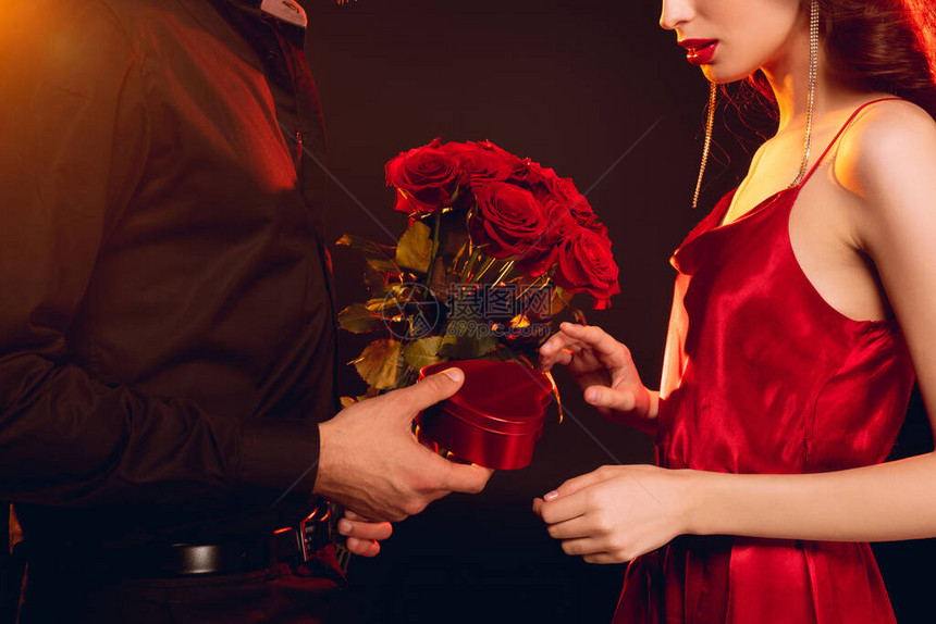 男人赠送礼物盒和玫瑰花束给有照明黑色背景的优雅女友图片