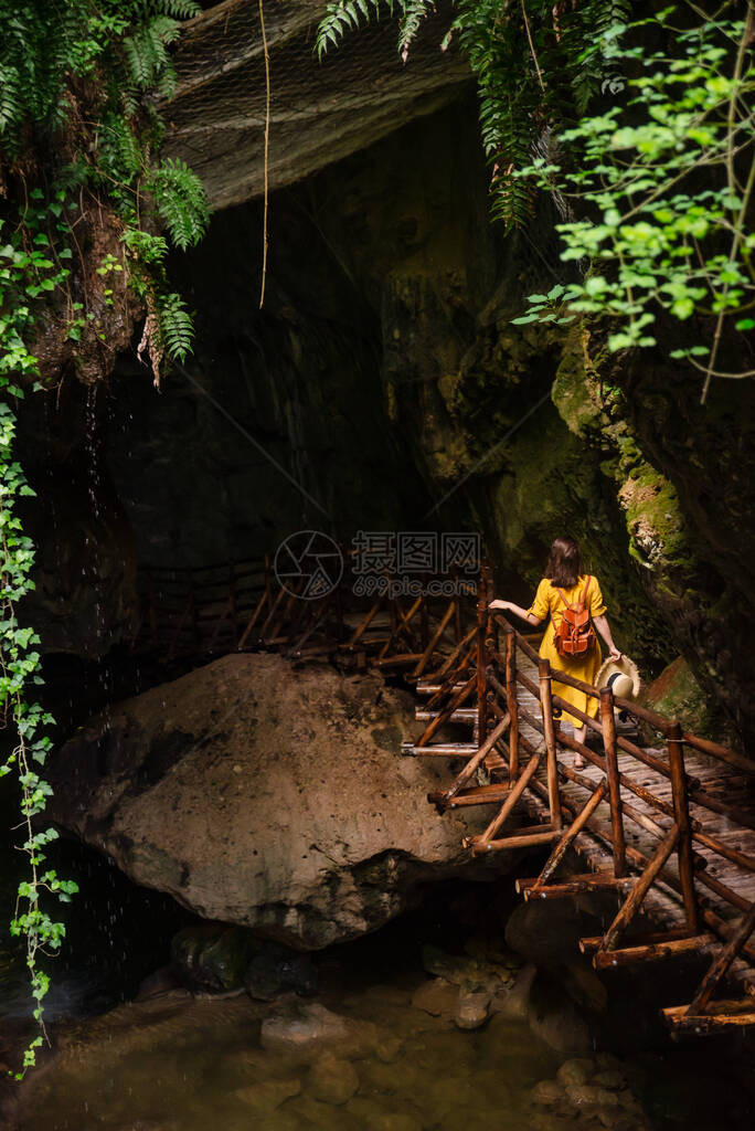 穿黄色太阳服的美女看着有河溪的洞穴旅行标图片