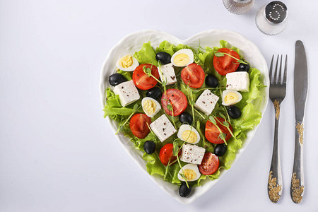 白色背景的心形盘子上放着樱桃番茄羊乳酪鹌鹑蛋橄榄和微绿蔬菜的健康沙拉图片