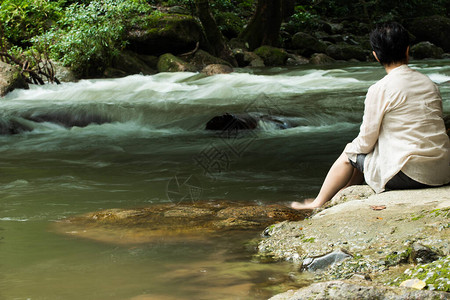 女人坐在瀑布河流急流附近的岩石上图片