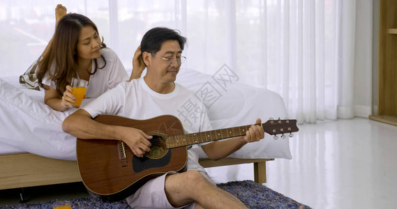 快乐的亚洲情人在卧室里一起弹吉他和唱歌图片