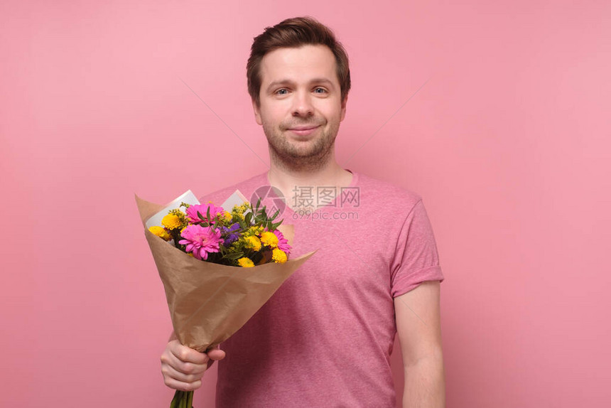 身穿粉色t恤的年轻白人男子拿着鲜花作为生日礼物送给母亲或女朋友周年纪念礼物的概念在彩色墙上图片