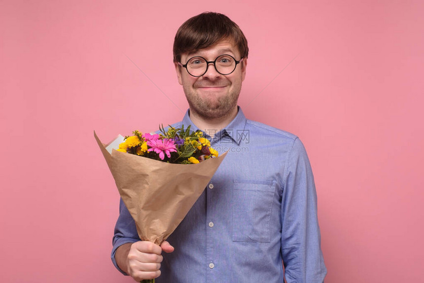 戴眼镜的年轻caucasian滑稽男子拿着鲜花作为生日礼物送给母亲或女朋友纪念周年的概念工作室在图片