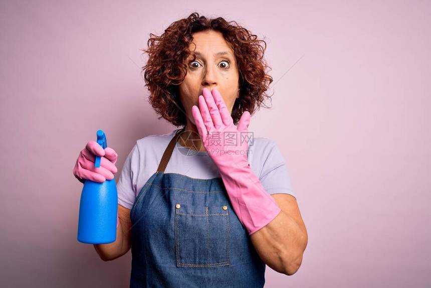 中年卷发妇女清洁做家务时穿着围裙和手套用喷雾器盖嘴用手震惊地为错误感到羞耻图片